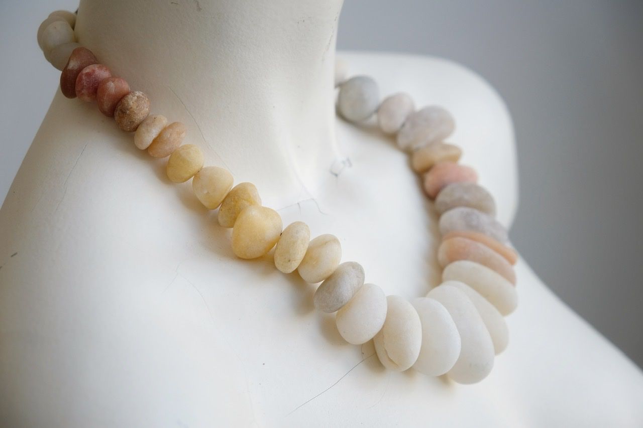 A white colored female formed mannequin wears a short necklace of ocean tumbled stones in white, yellow, pale pink and red