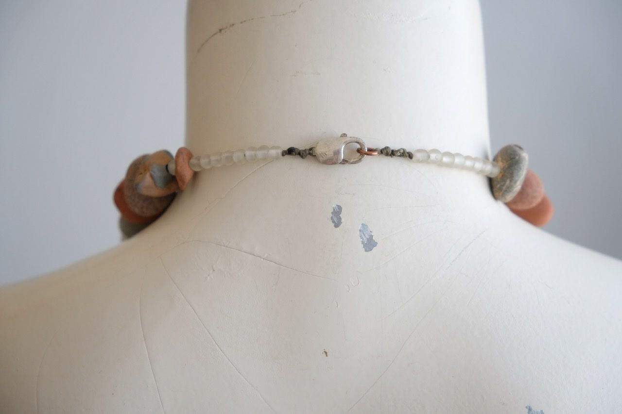 A white female form mannequin wears a sculptural necklace of ocean tumbled stones In greys, brown, red and white