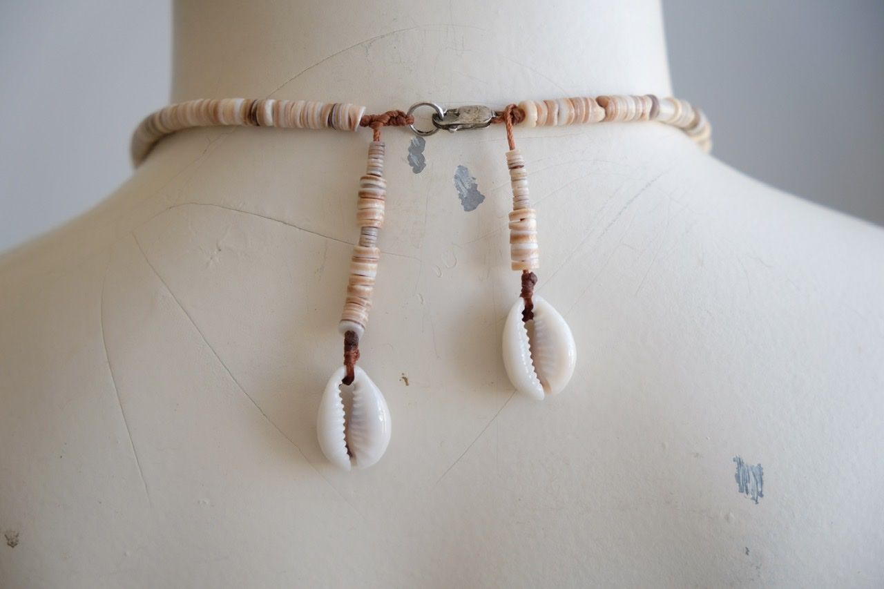 A white female form mannequin wears a sculptural necklace of ocean tumbled stones In greys, brown, red and white