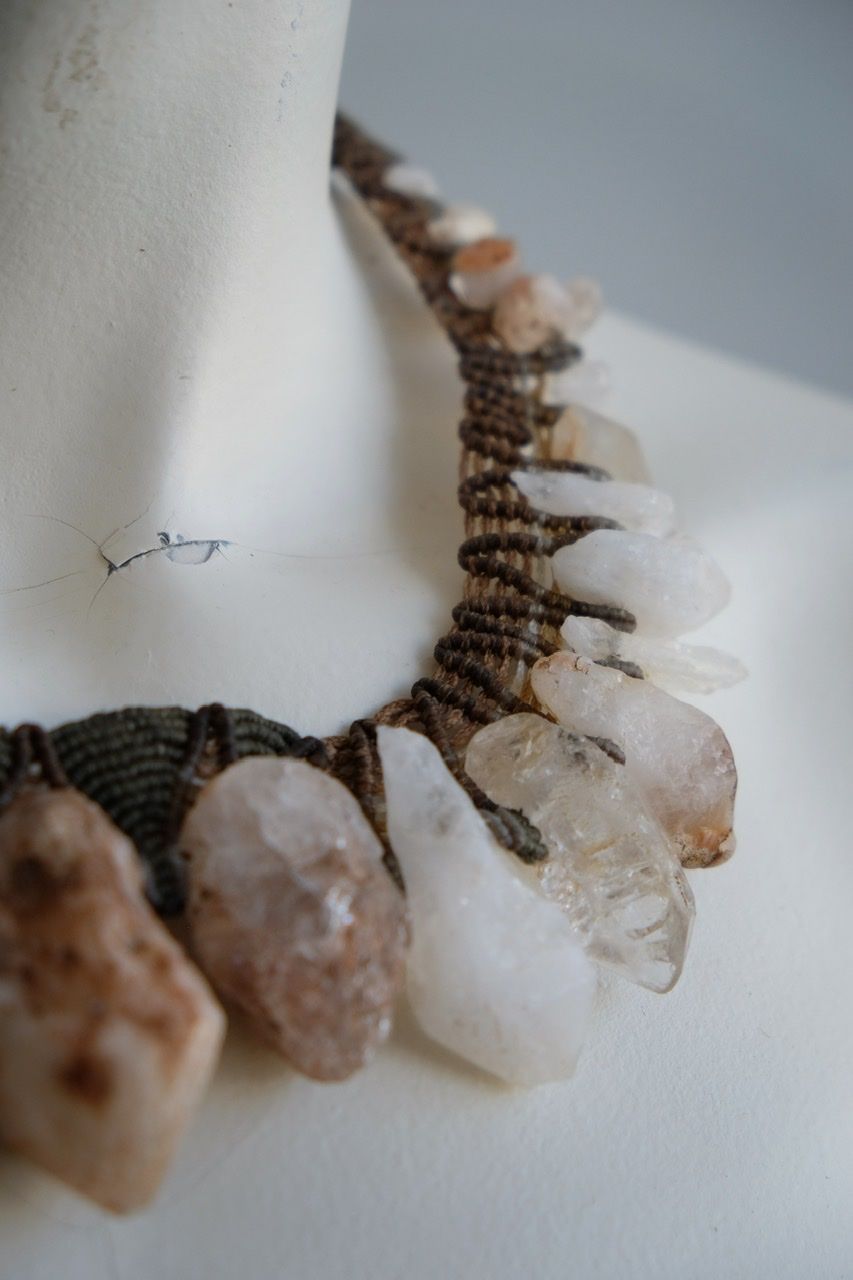 A white colored female form mannequin wears a sculptural necklace of rough quartz points and brown and green knotwork