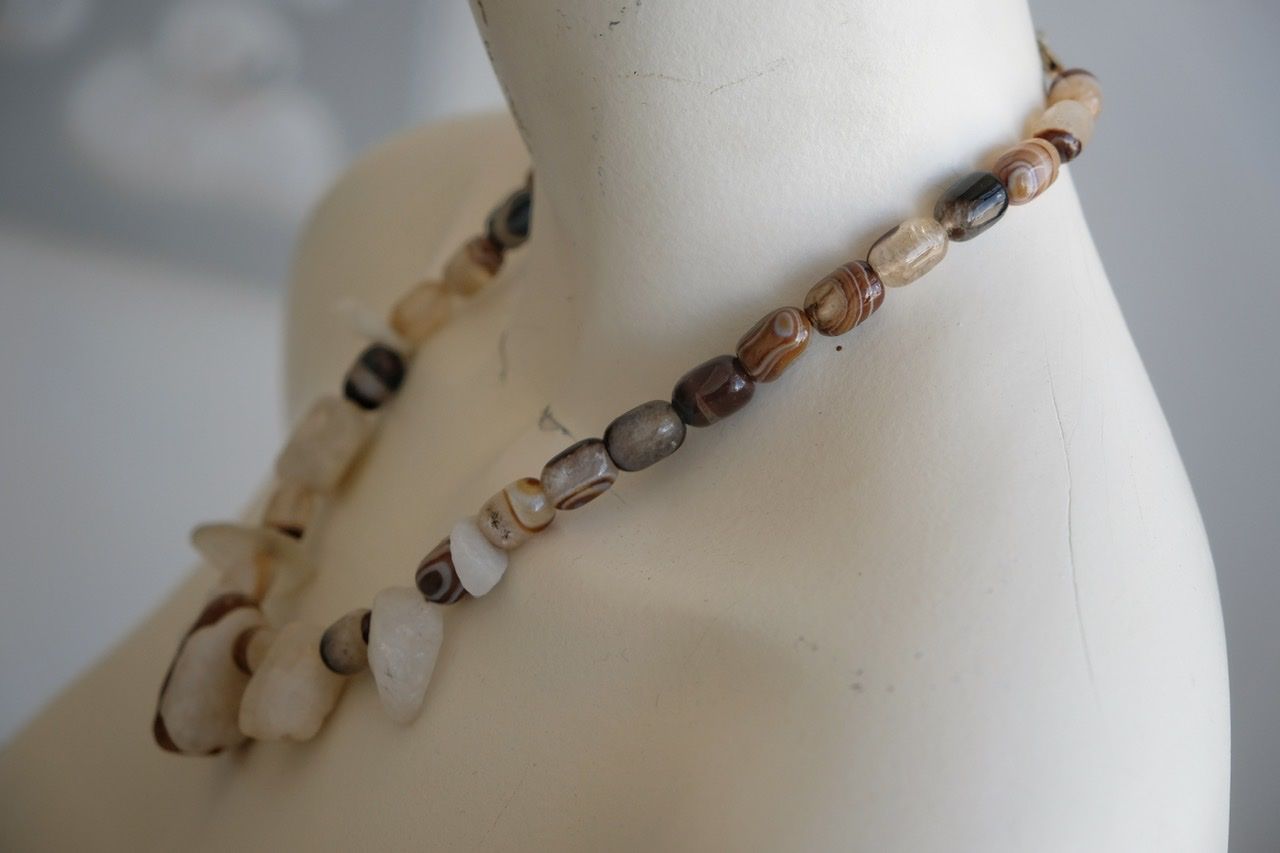 A white colored female form mannequin wears a white, clear and brown necklace of agate, Quartz and tumbled glass
