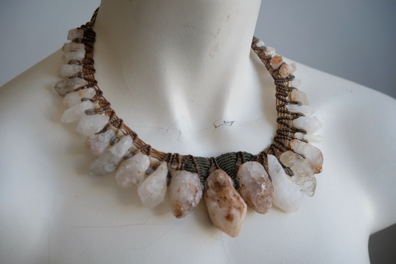 A white colored female form mannequin wears a sculptural necklace of rough quartz points and brown and green knotwork