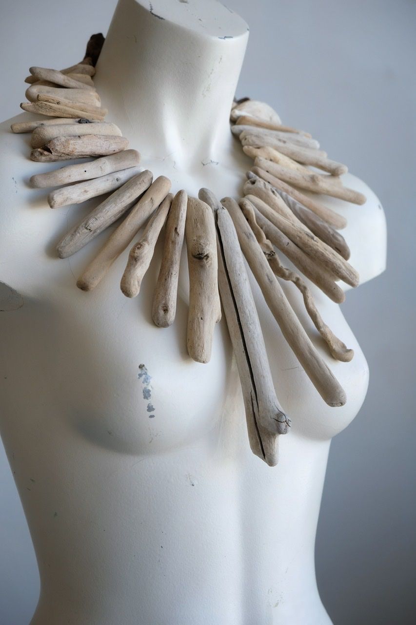 A white female form mannequin wears a sculptural necklace of light colored drift wood