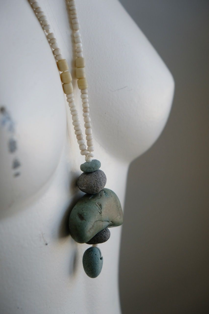 A white colored female form mannequin wears a sculptural necklace of blue green river tumbled stones and white glass beads