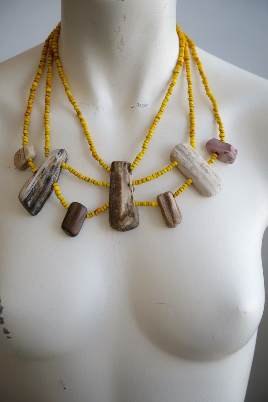 A white colored female form mannequin wears a three strand sculptural necklace of petrified wood and yellow glass beads