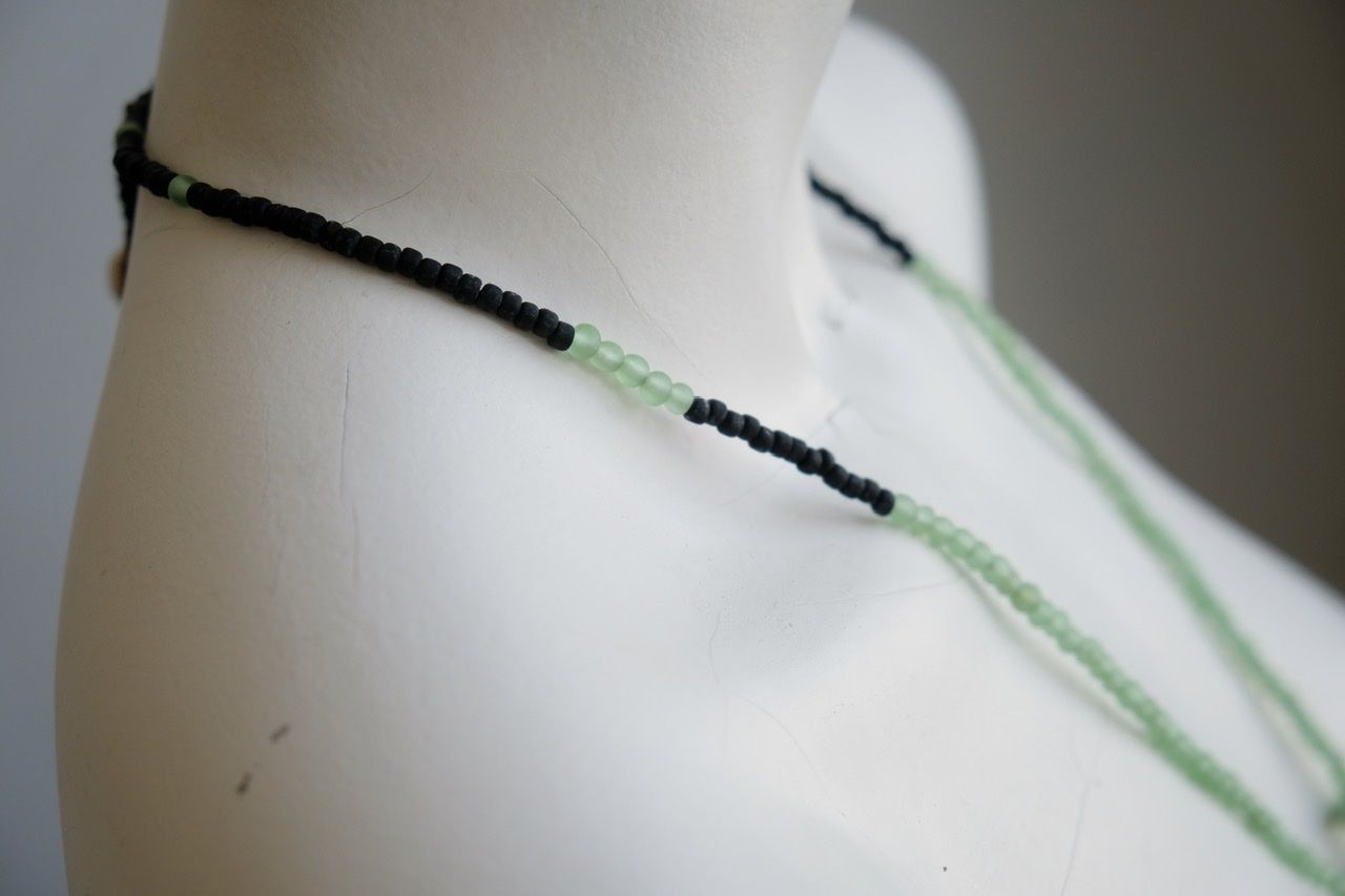 A white female form mannequin wears a necklace of a green ocean tumbled stone with green and black beads