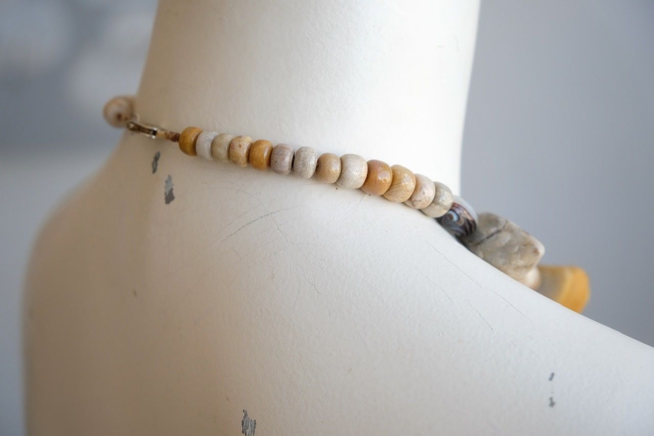 A white color female form mannequin wears a sculptural stone necklace in toffee, cream and yellow colors 