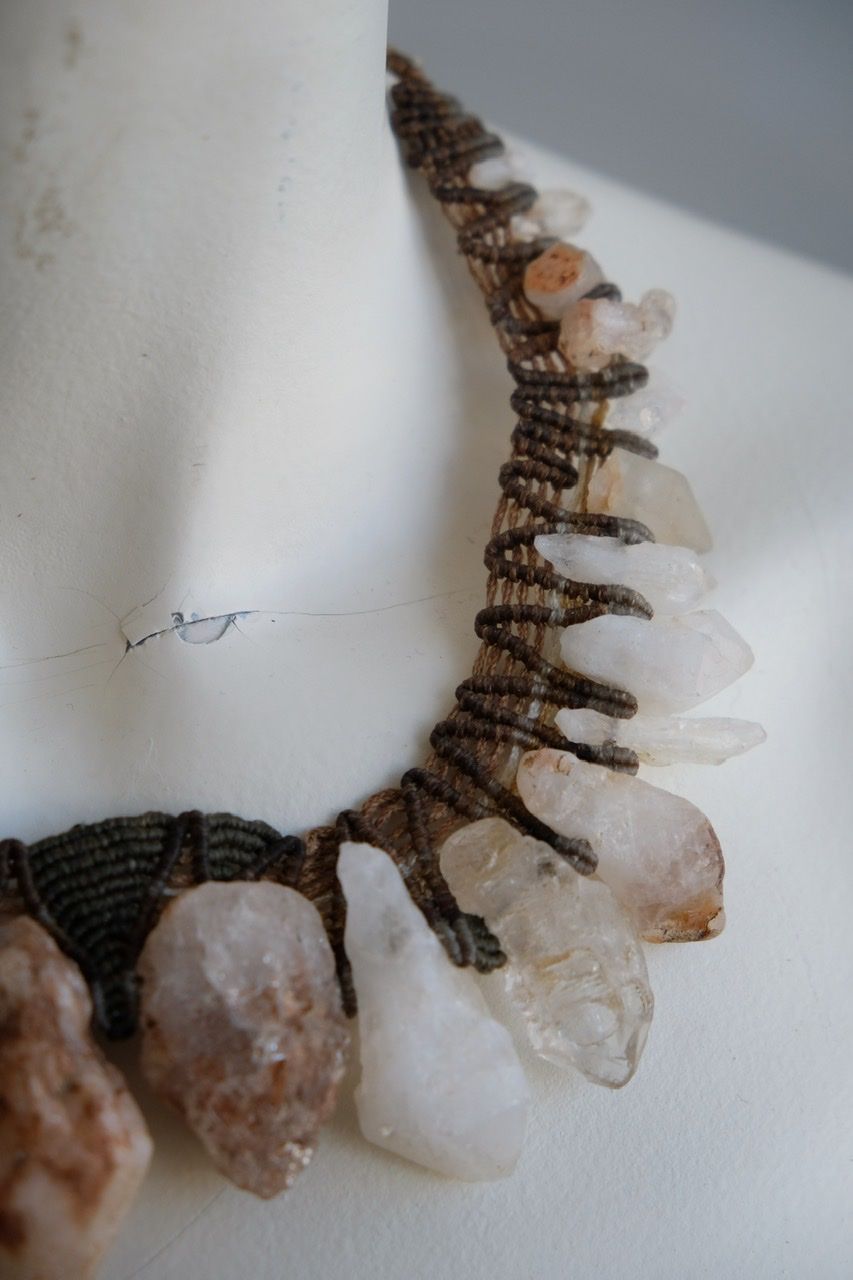 A white colored female form mannequin wears a sculptural necklace of rough quartz points and brown and green knotwork