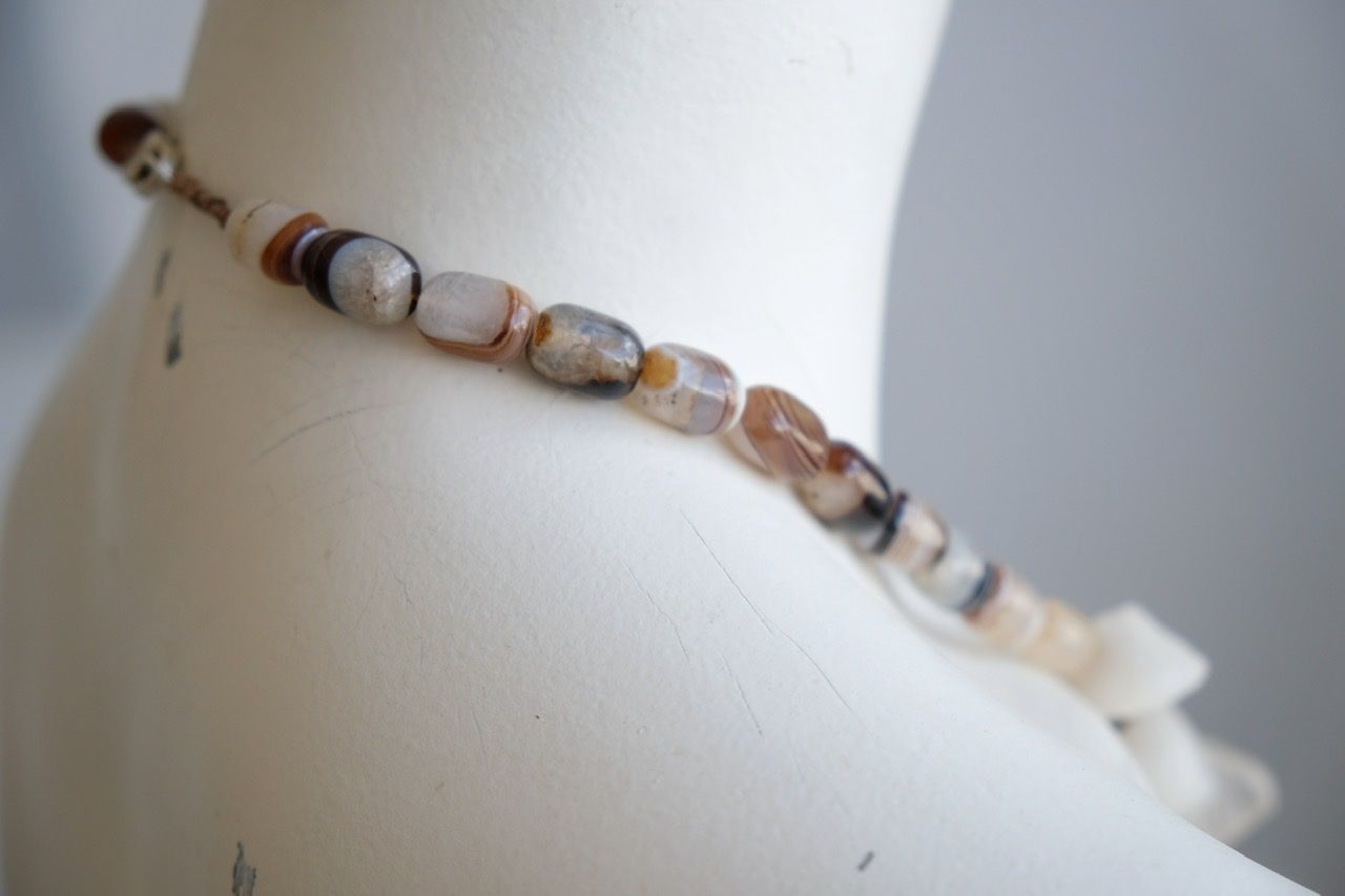 A white colored female form mannequin wears a white, clear and brown necklace of agate, Quartz and tumbled glass