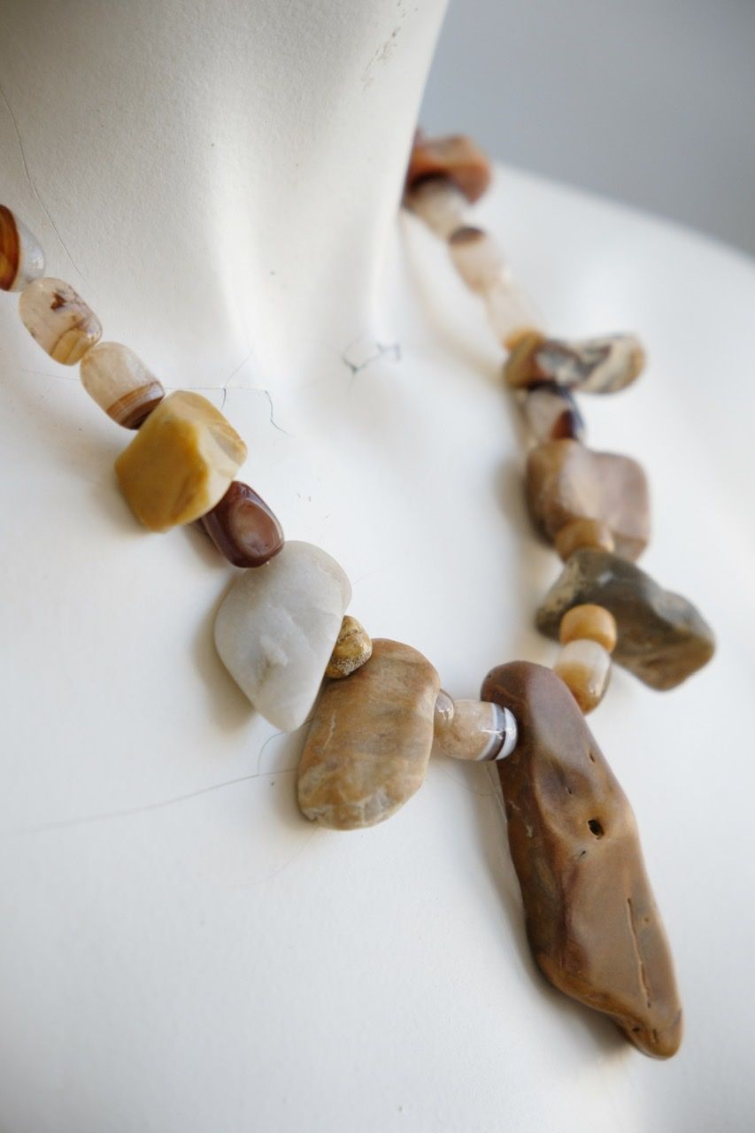 A white color female form mannequin wears a sculptural stone necklace in toffee, cream and yellow colors 