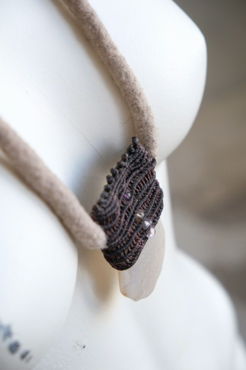 A white colored female form mannequin wears a sculptural necklace of a light grey felted cord, dark purple basket with a white chalcedony stone