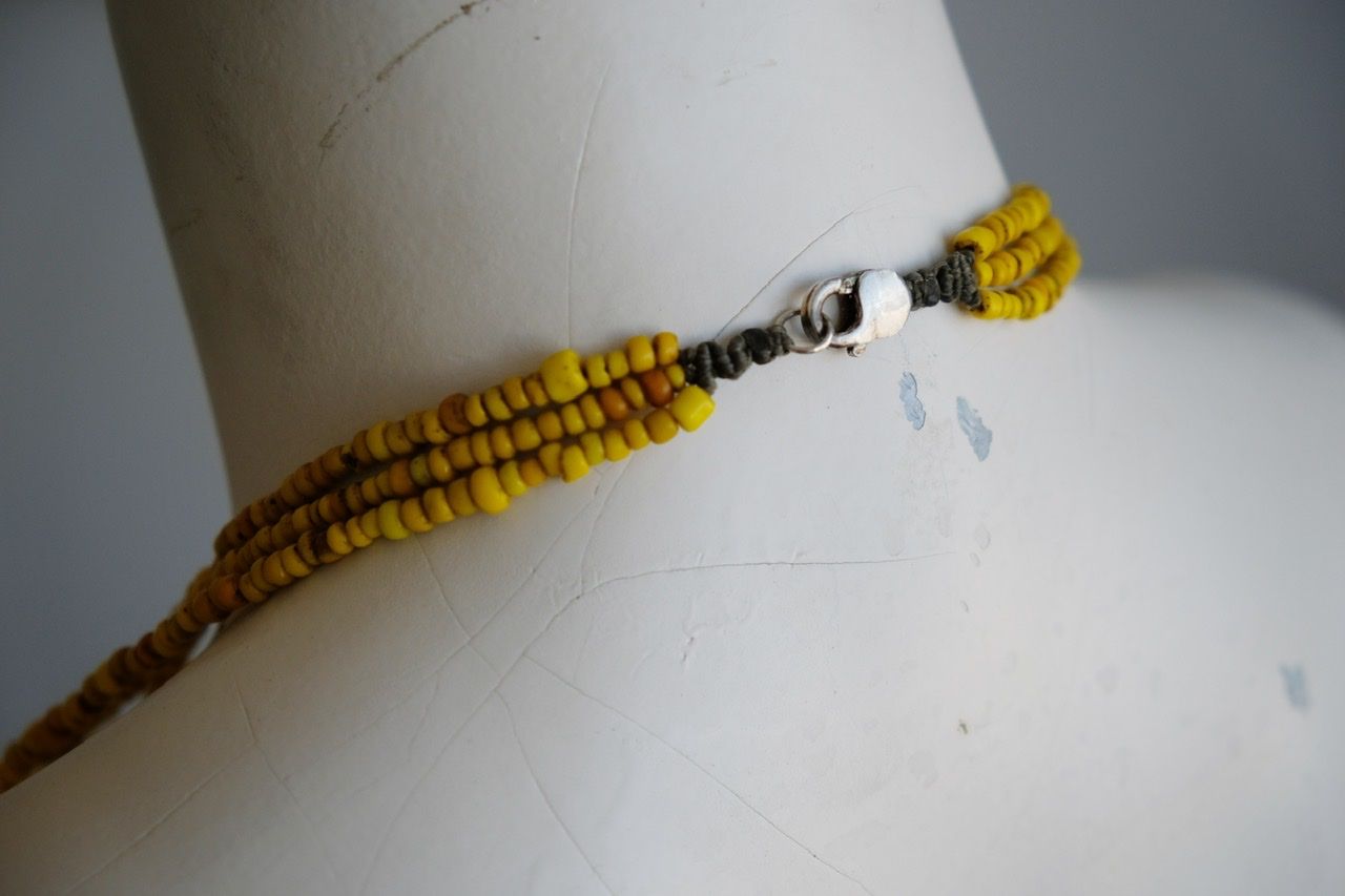 A white colored female form mannequin wears a three strand sculptural necklace of petrified wood and yellow glass beads