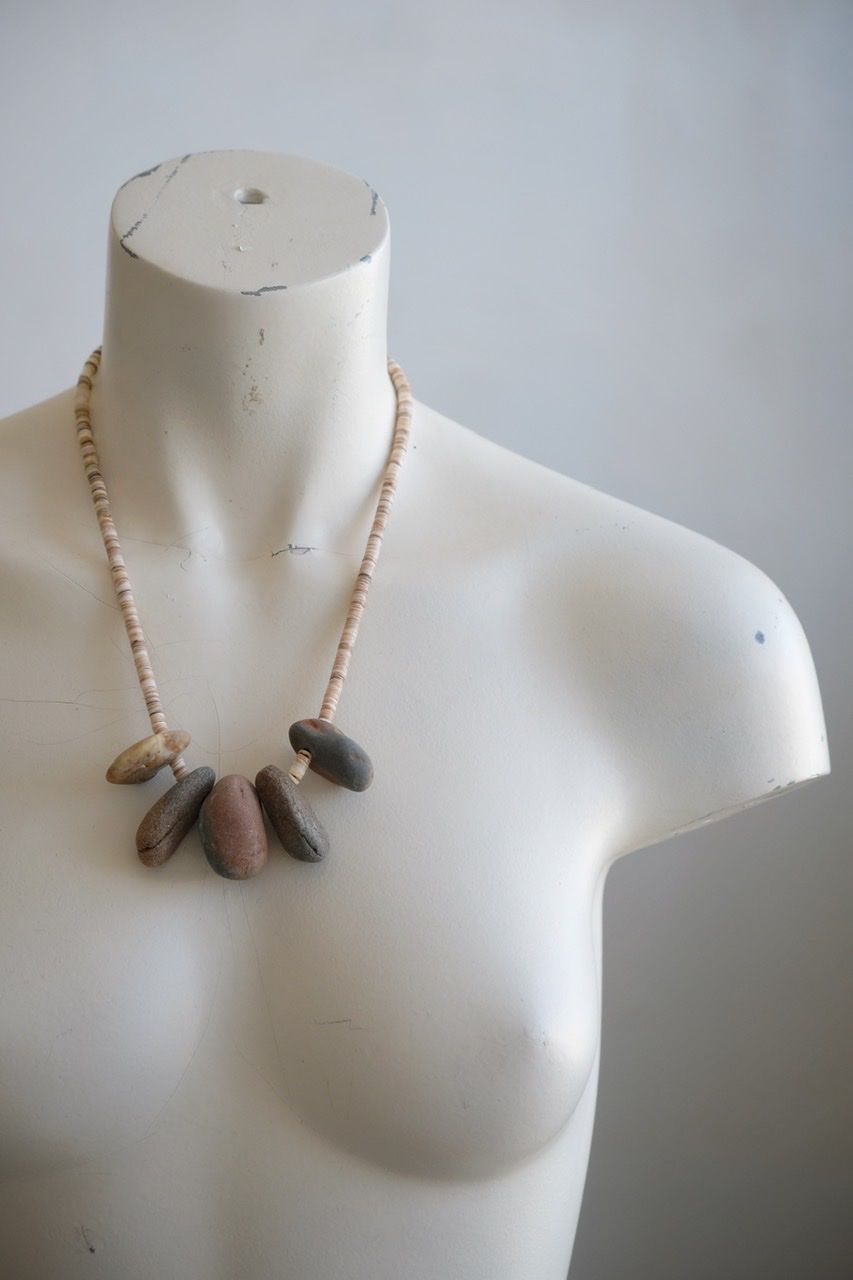 A white female form mannequin wears a sculptural necklace of ocean tumbled stones In greys, brown, red and white