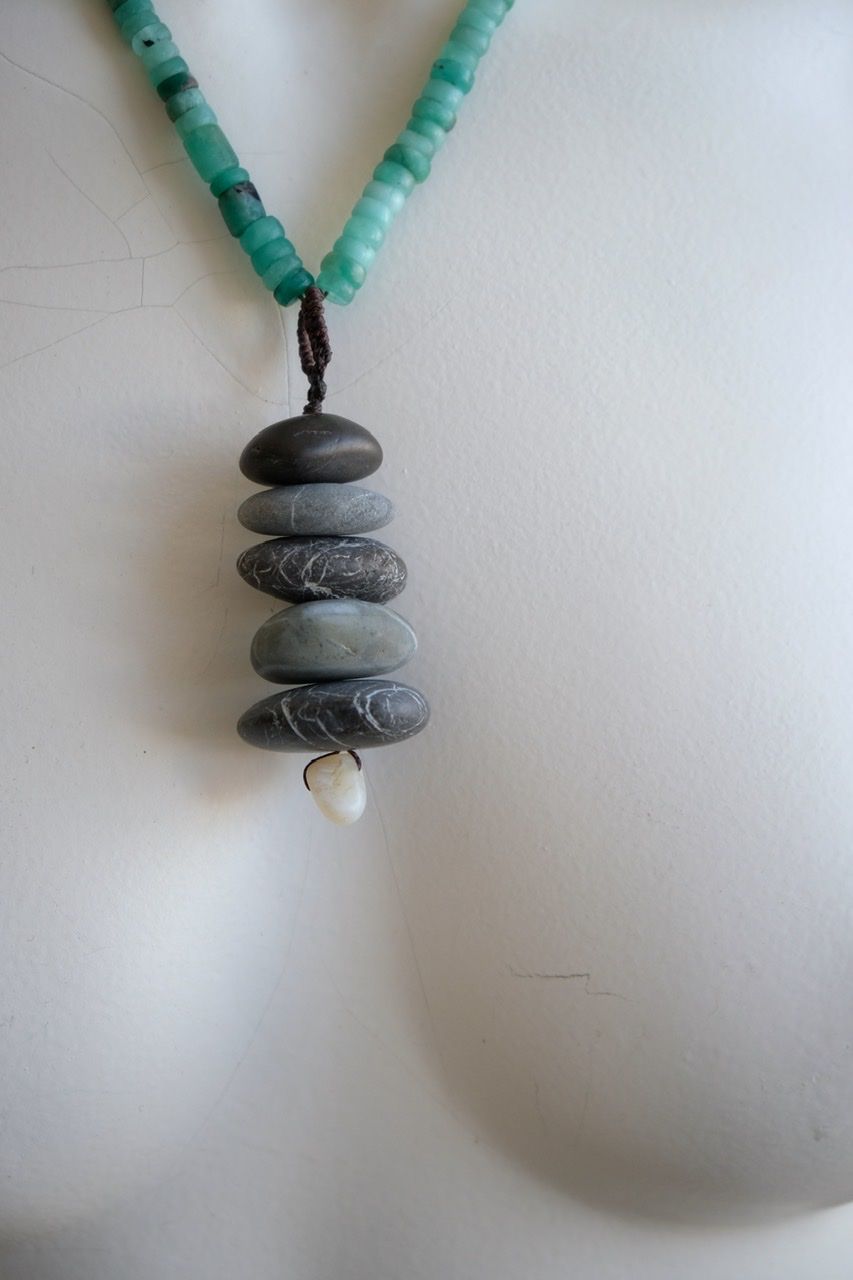 A white color female form mannequin wears a sculptural necklace of smooth dark blue grey stones In the form of a tiny cairn