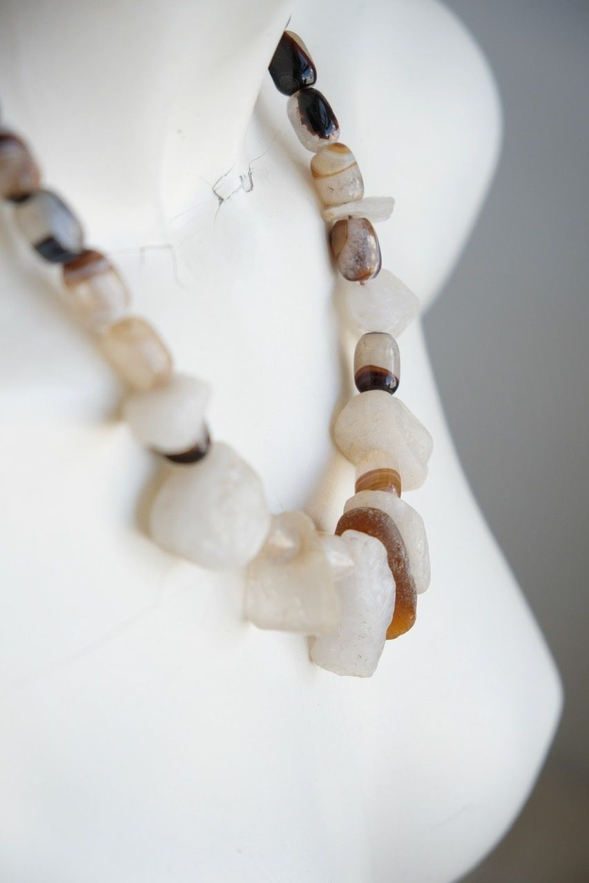 A white colored female form mannequin wears a white, clear and brown necklace of agate, Quartz and tumbled glass
