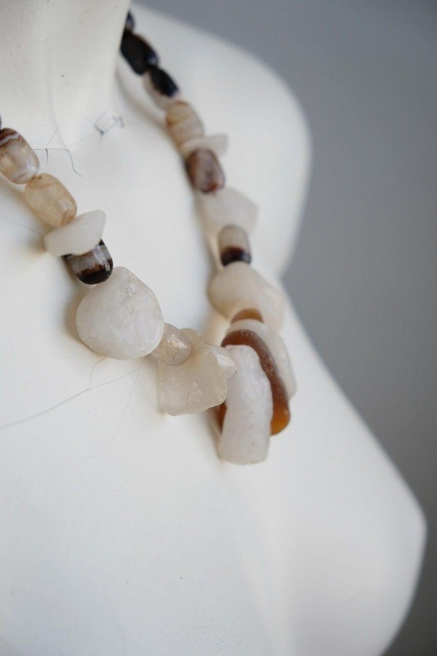 A white colored female form mannequin wears a white, clear and brown necklace of agate, Quartz and tumbled glass