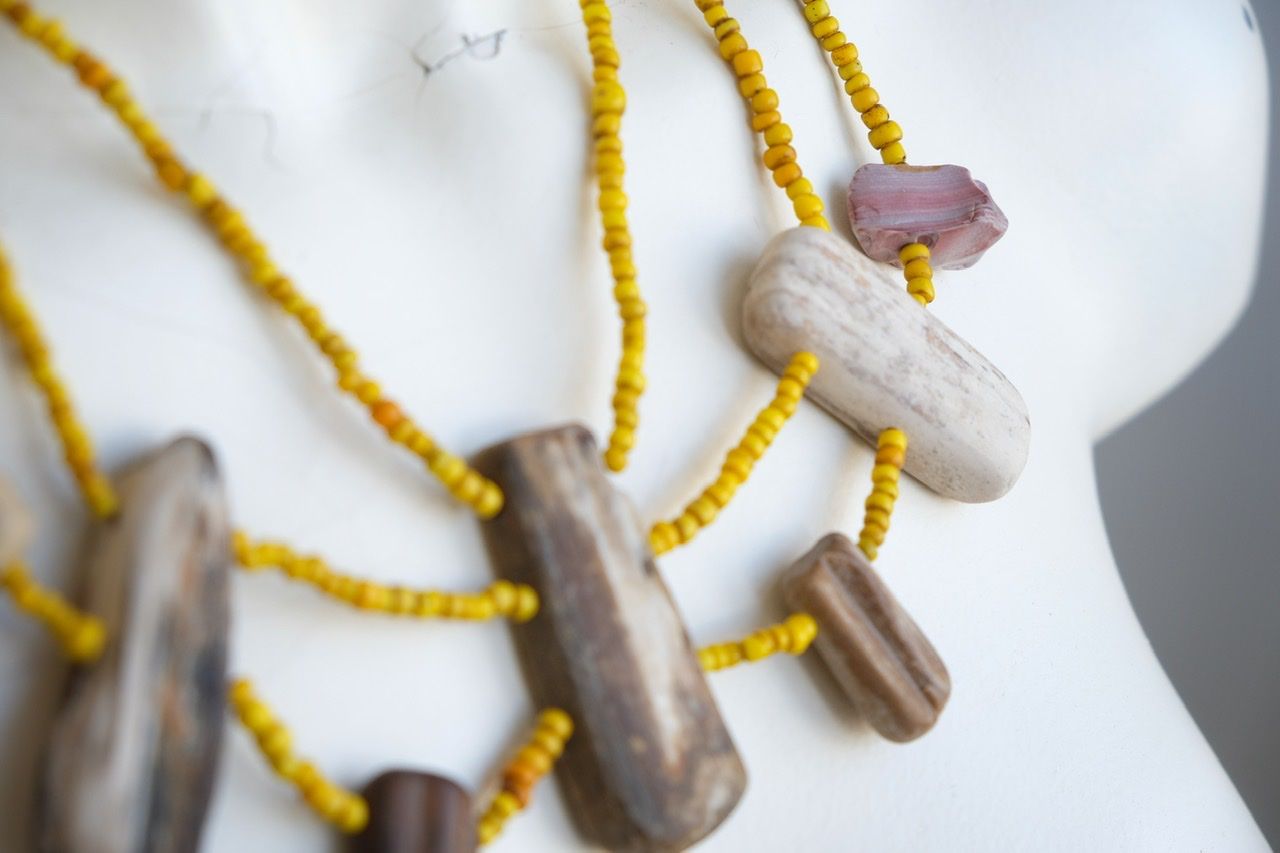 A white colored female form mannequin wears a three strand sculptural necklace of petrified wood and yellow glass beads