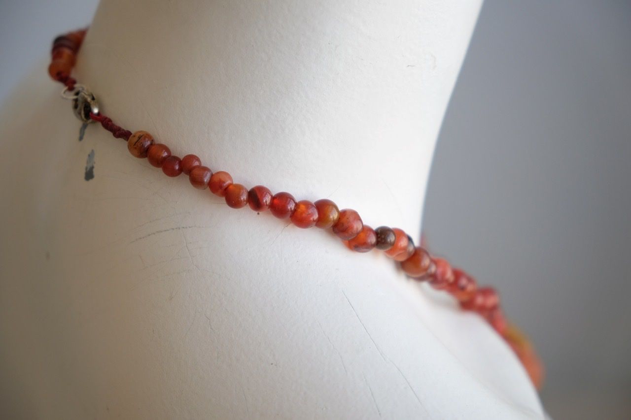 A white color female form mannequin wears a sculptural stone necklace in red, orange and yellow ochre colors 