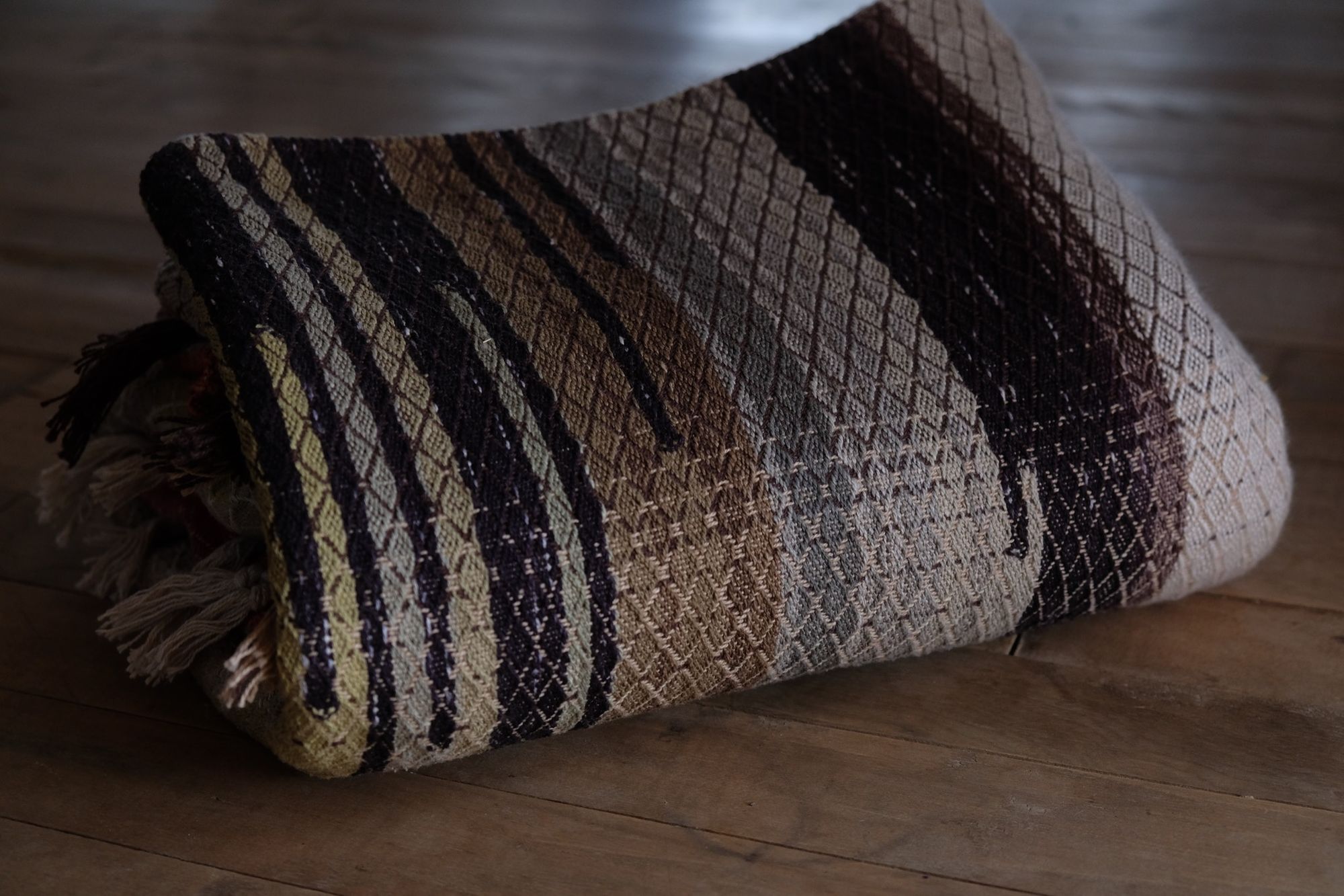 geometric shaped, natural and rainbow colored handwoven, diamond pattern fabric on a wooden floor, folded