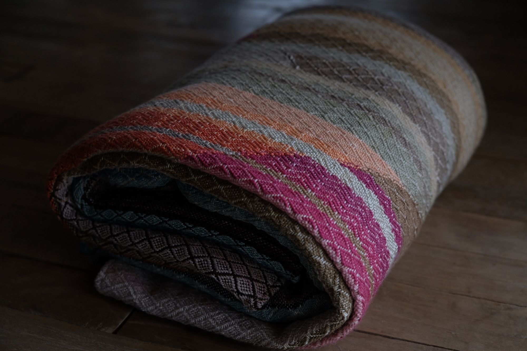 geometric shaped, natural and rainbow colored handwoven, diamond pattern fabric on a wooden floor, folded