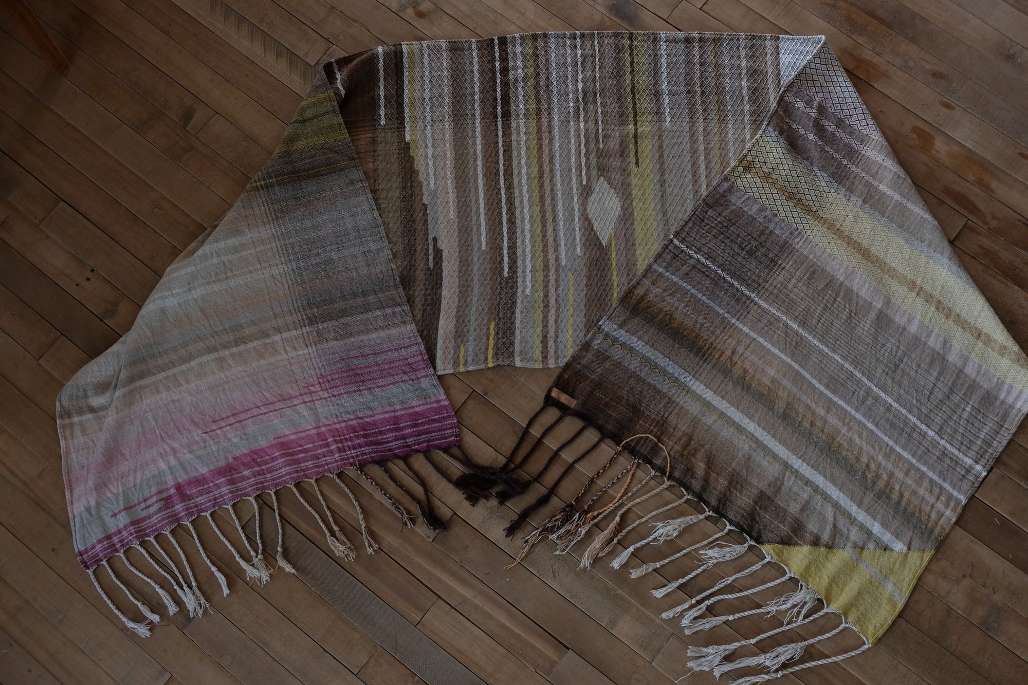handwoven diamond pattern and geometric details in browns, tan, yellows, whites and pinks laying on a wooden floor