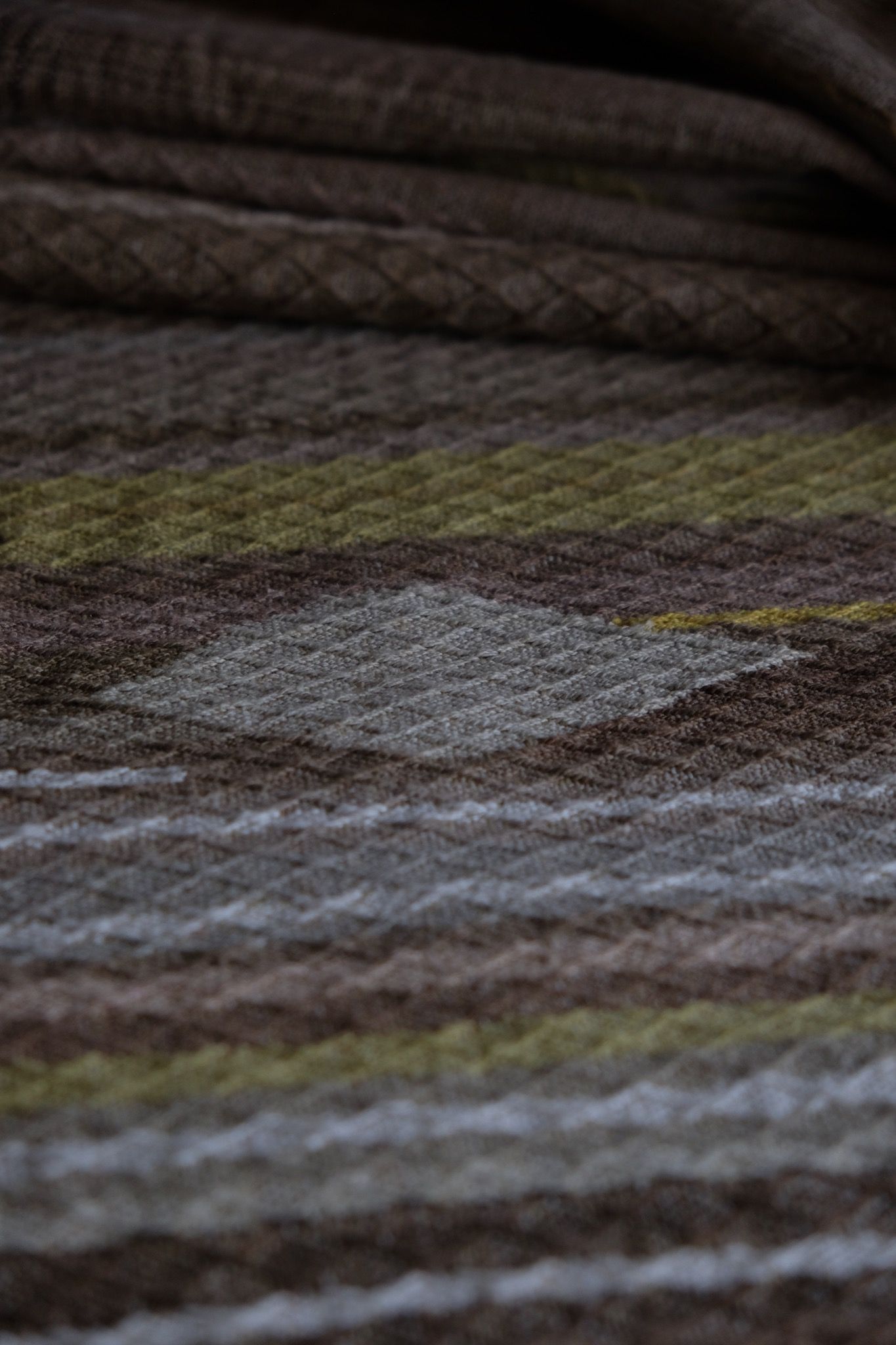 detail of handwoven diamond pattern and geometric details in browns, tan, yellows, whites and pinks laying on a wooden floor