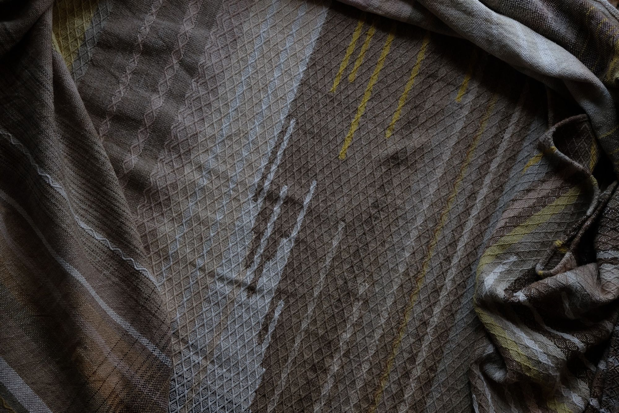 detail of handwoven diamond pattern and geometric details in browns, tan, yellows, whites and pinks laying on a wooden floor