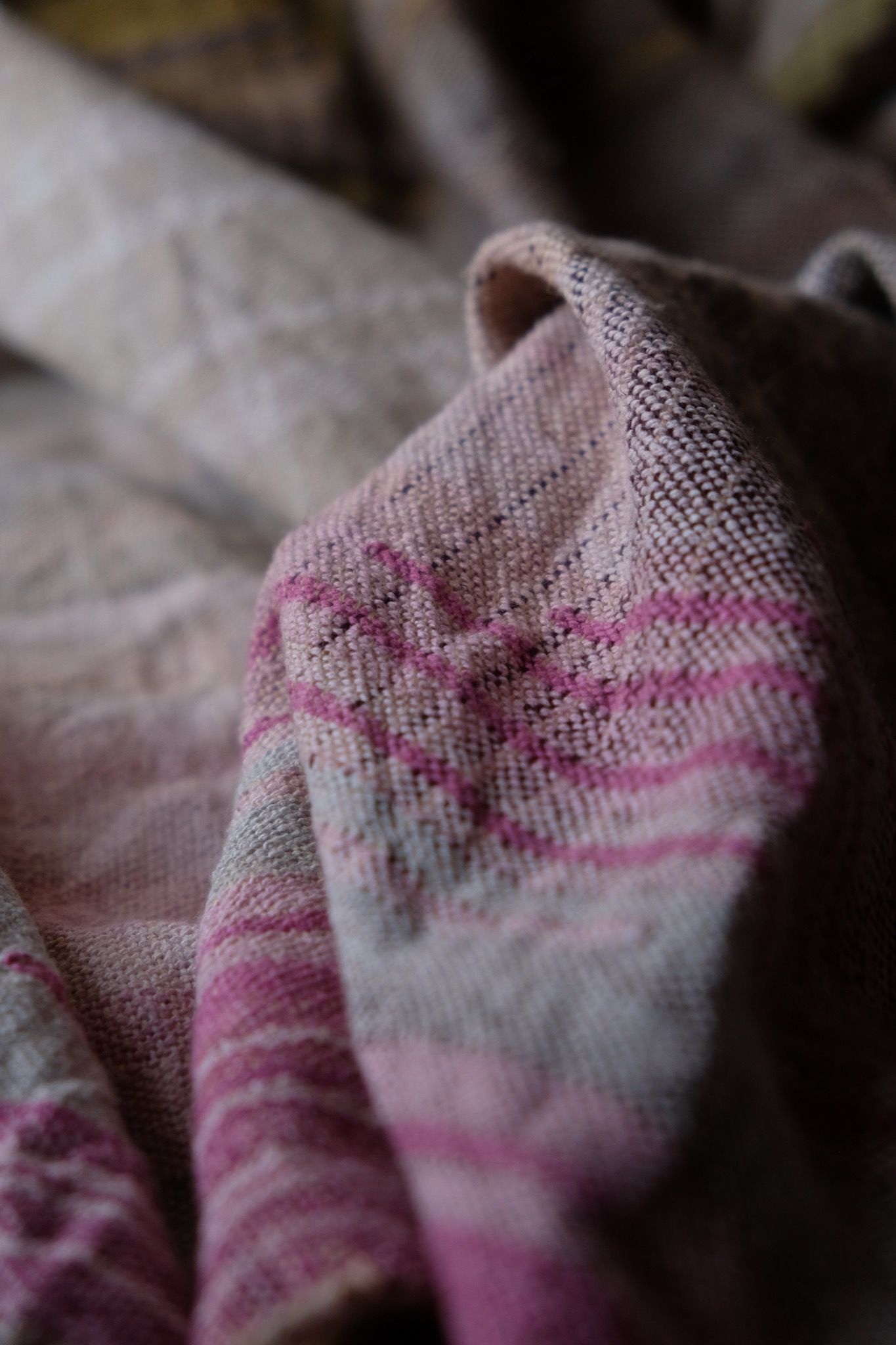 detail of handwoven diamond pattern and geometric details in browns, tan, yellows, whites and pinks laying on a wooden floor