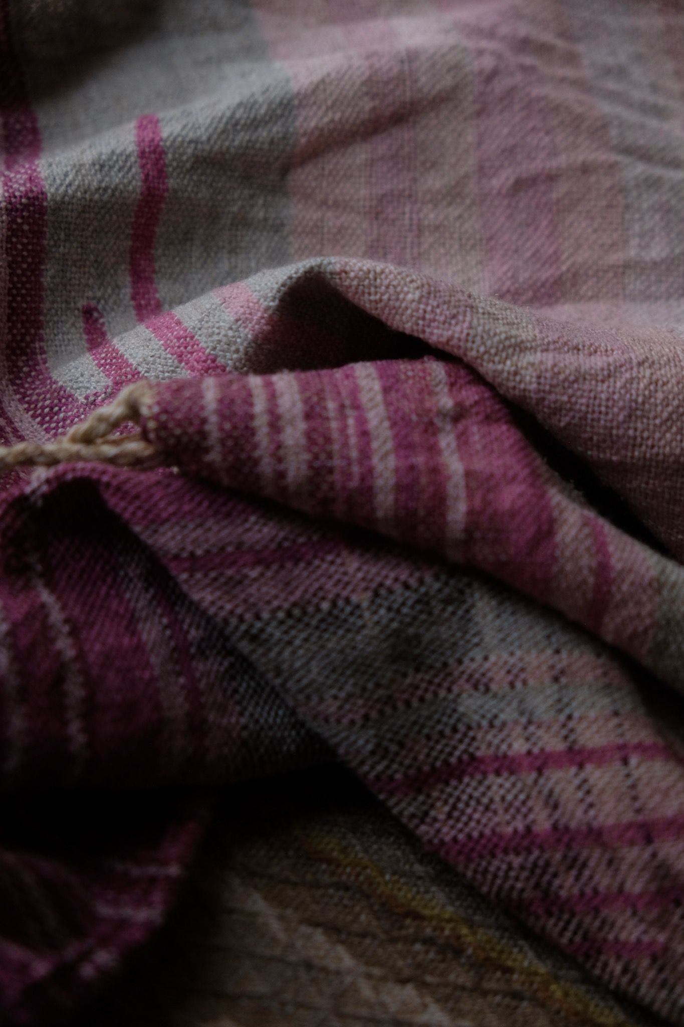 detail of handwoven diamond pattern and geometric details in browns, tan, yellows, whites and pinks laying on a wooden floor