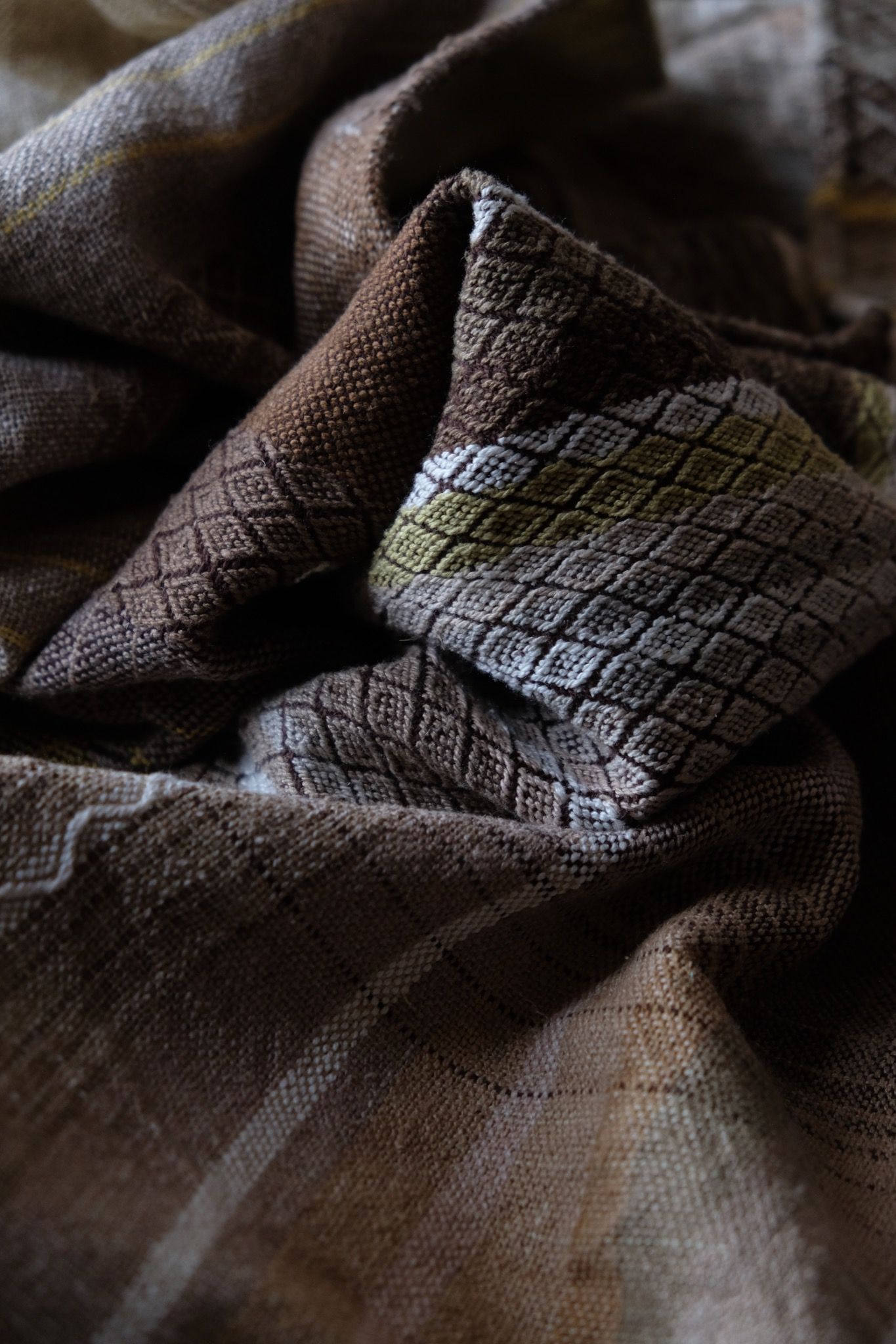 detail of handwoven diamond pattern and geometric details in browns, tan, yellows, whites and pinks laying on a wooden floor