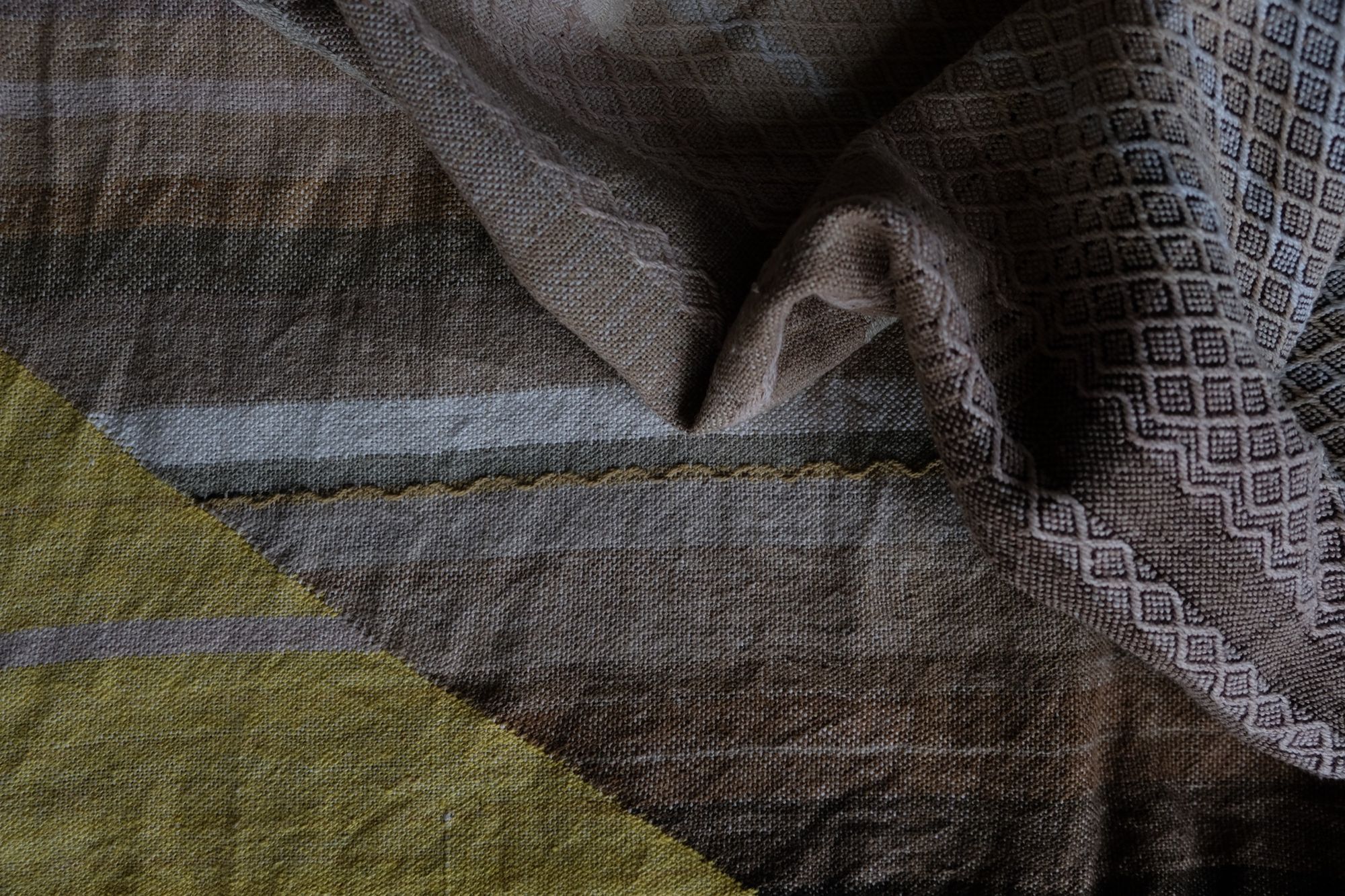 detail of handwoven diamond pattern and geometric details in browns, tan, yellows, whites and pinks laying on a wooden floor