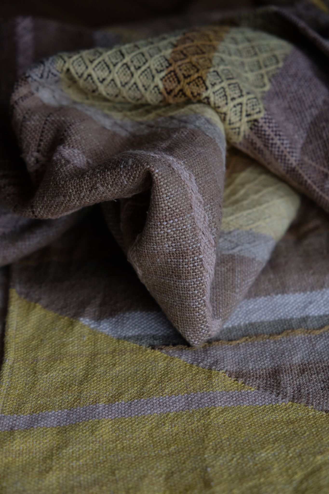 detail of handwoven diamond pattern and geometric details in browns, tan, yellows, whites and pinks laying on a wooden floor