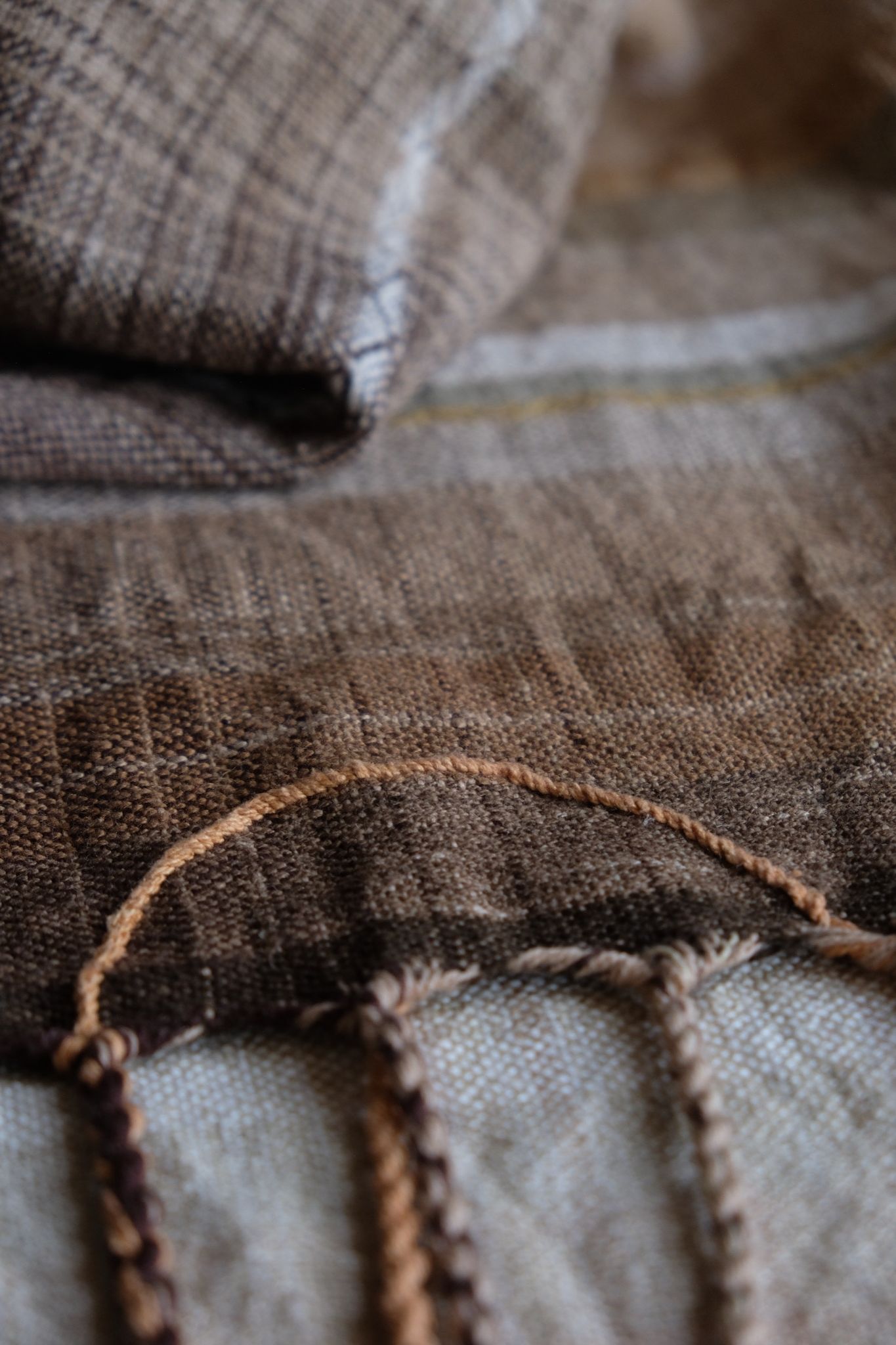 detail of handwoven diamond pattern and geometric details in browns, tan, yellows, whites and pinks laying on a wooden floor