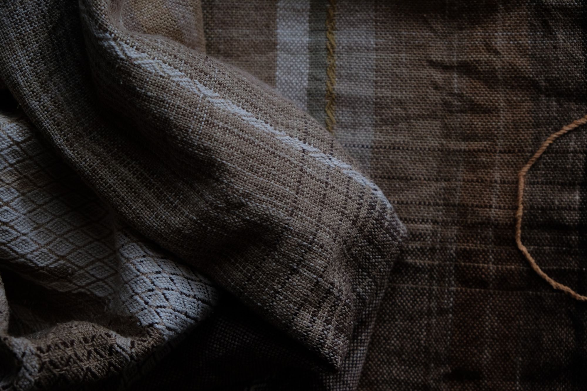 detail of handwoven diamond pattern and geometric details in browns, tan, yellows, whites and pinks laying on a wooden floor