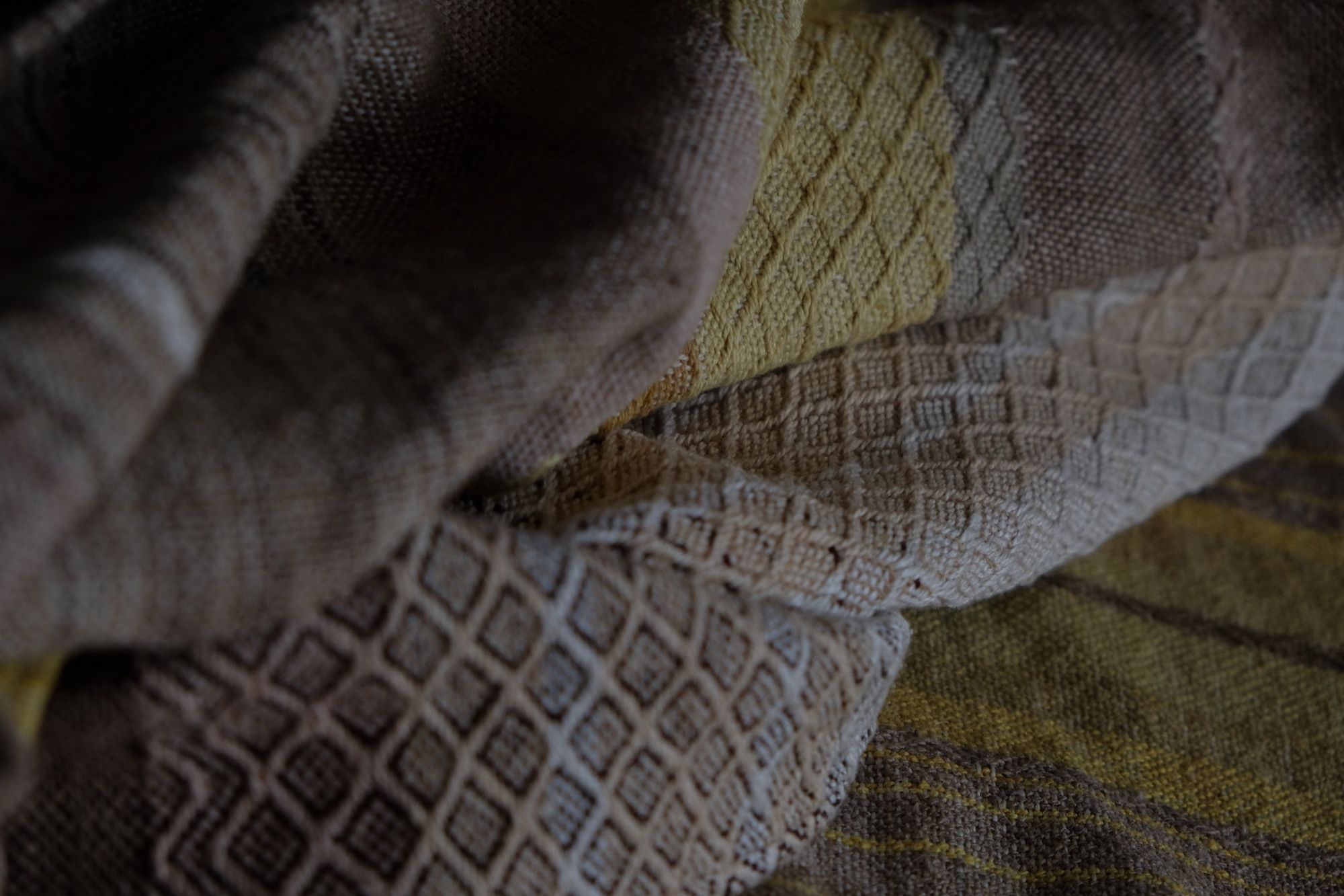 detail of handwoven diamond pattern and geometric details in browns, tan, yellows, whites and pinks laying on a wooden floor