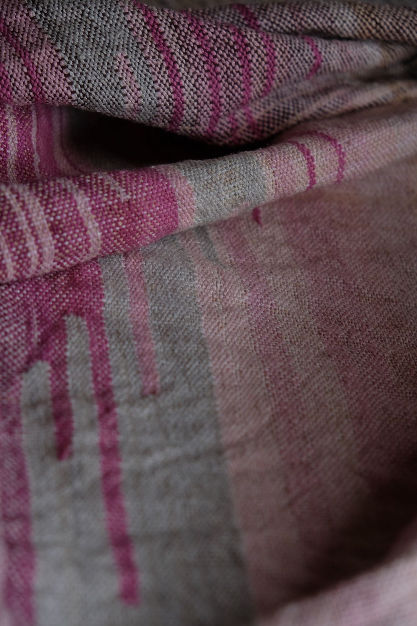 detail of handwoven diamond pattern and geometric details in browns, tan, yellows, whites and pinks laying on a wooden floor