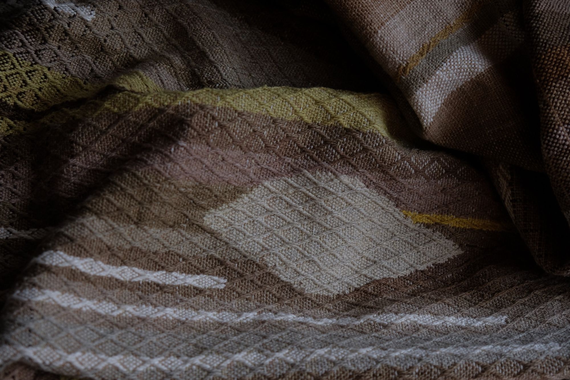 detail of handwoven diamond pattern and geometric details in browns, tan, yellows, whites and pinks laying on a wooden floor