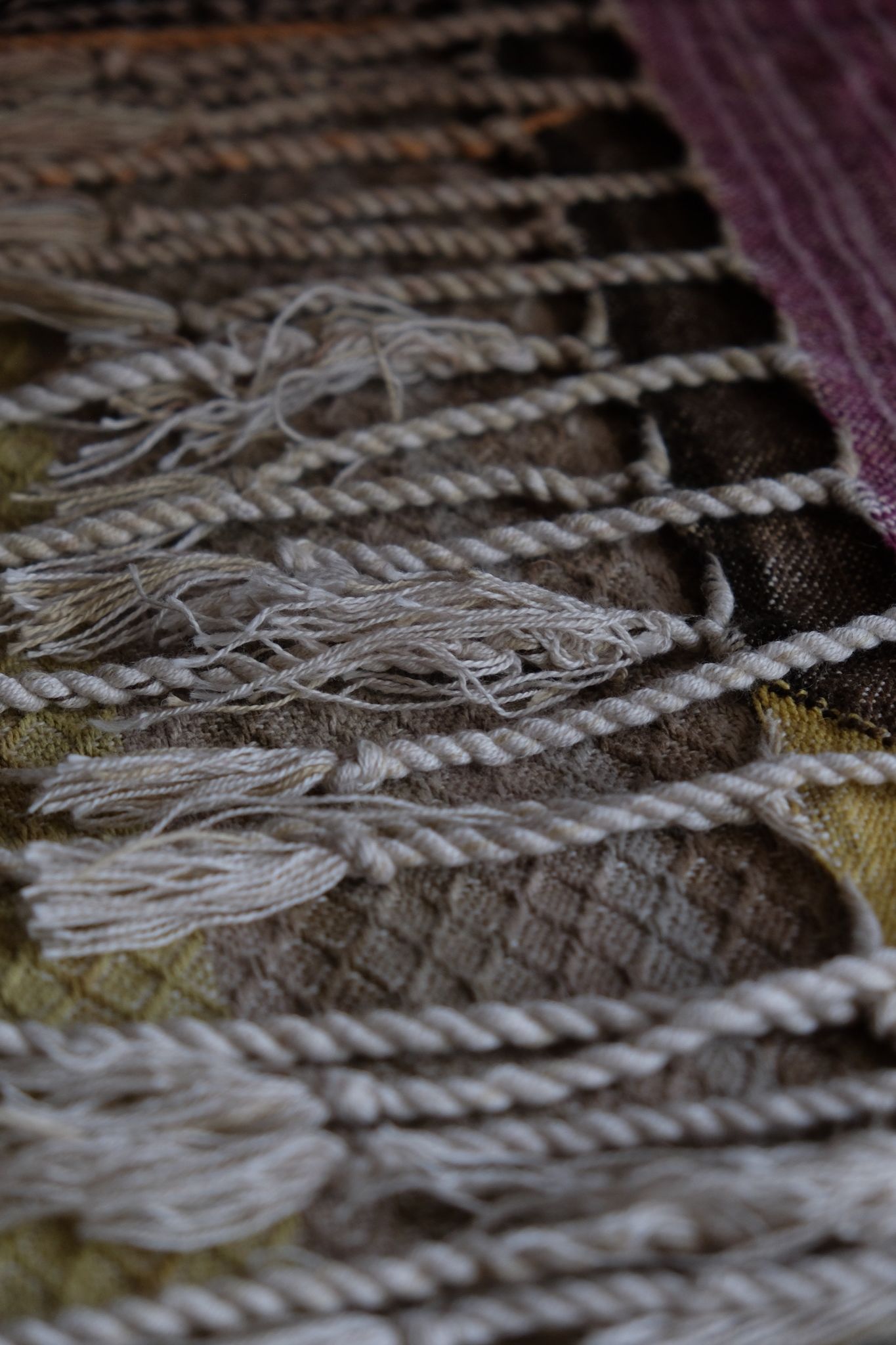 detail of handwoven diamond pattern and geometric details in browns, tan, yellows, whites and pinks laying on a wooden floor