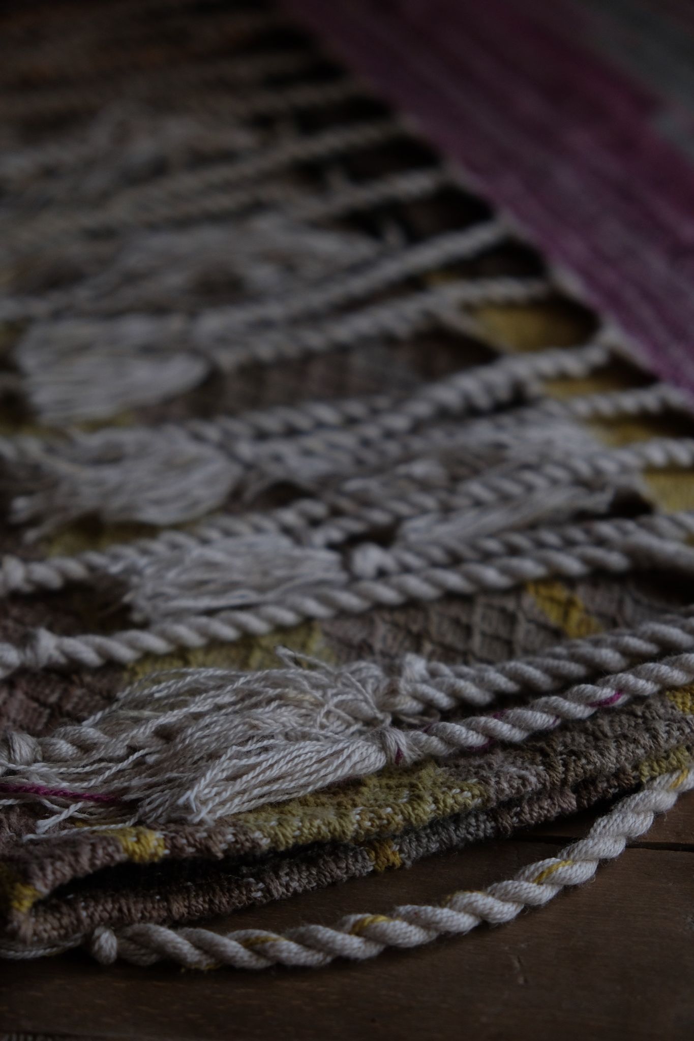 detail of handwoven diamond pattern and geometric details in browns, tan, yellows, whites and pinks laying on a wooden floor