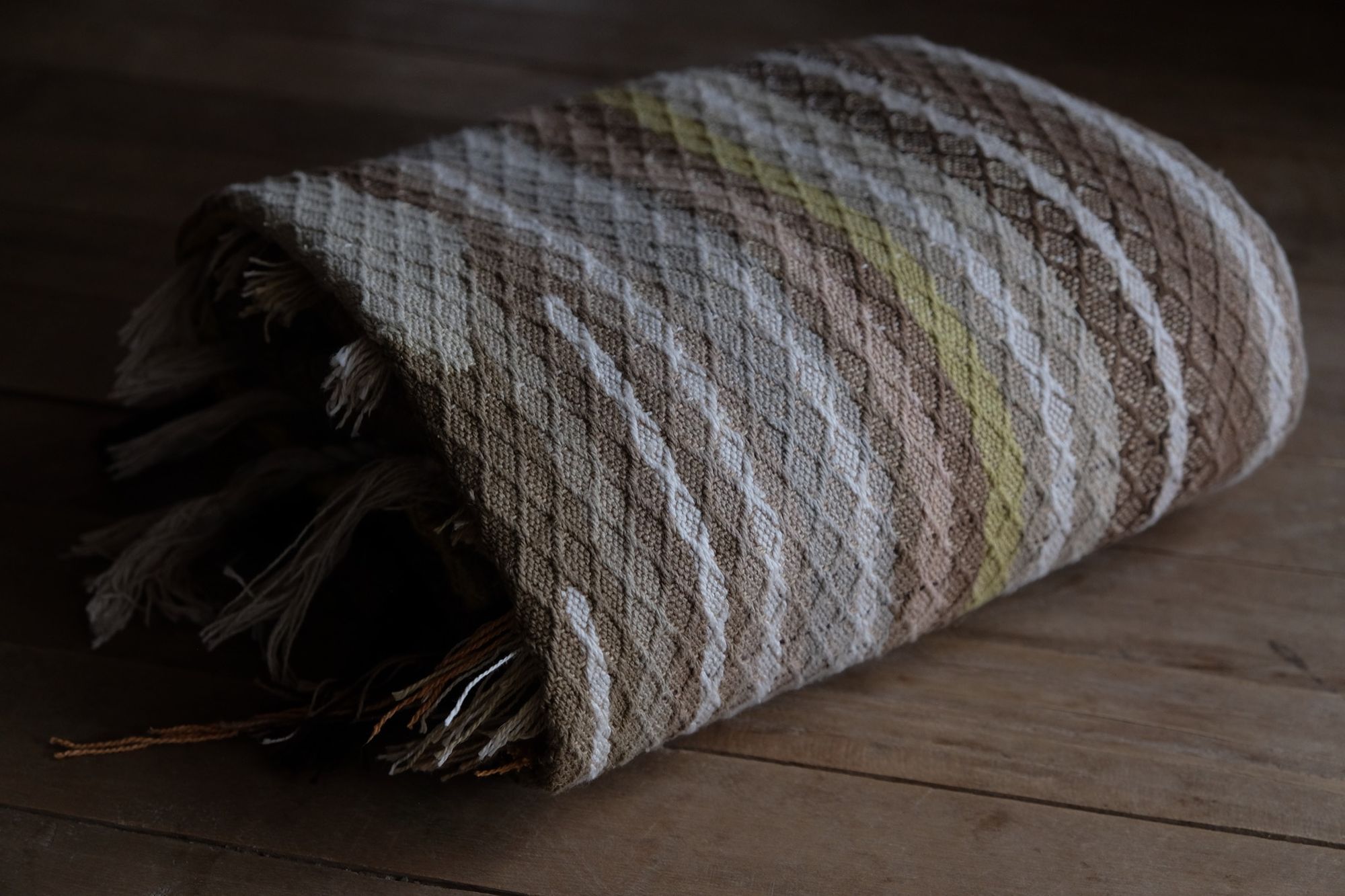detail of handwoven diamond pattern and geometric details in browns, tan, yellows, whites and pinks laying on a wooden floor