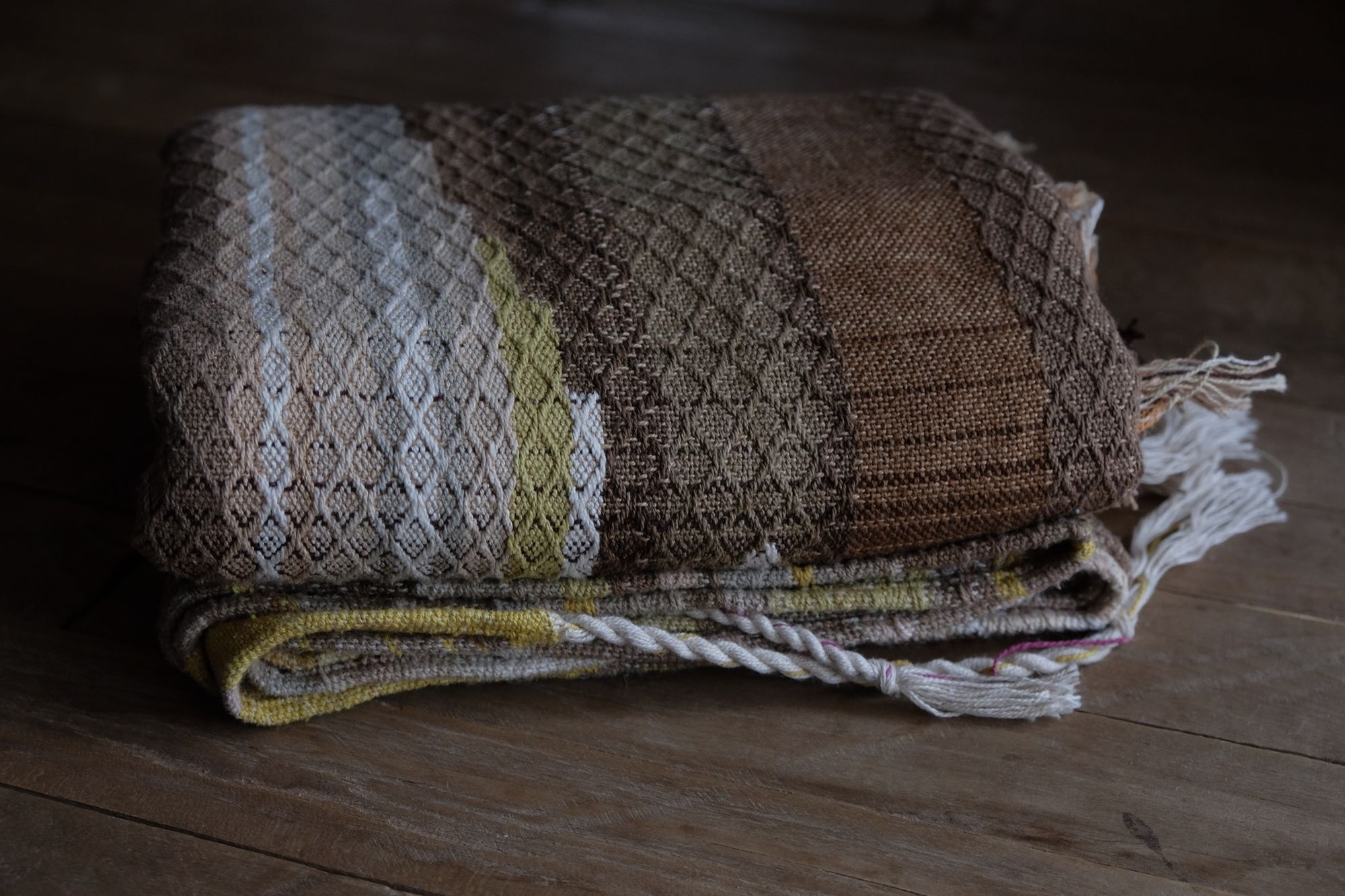 detail of handwoven diamond pattern and geometric details in browns, tan, yellows, whites and pinks laying on a wooden floor