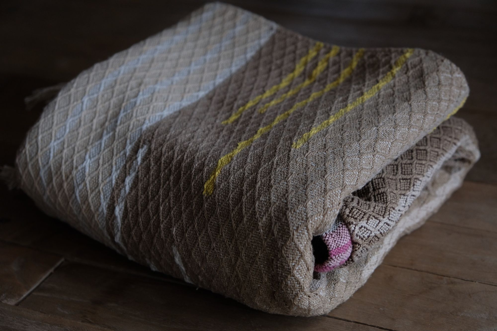 detail of handwoven diamond pattern and geometric details in browns, tan, yellows, whites and pinks laying on a wooden floor