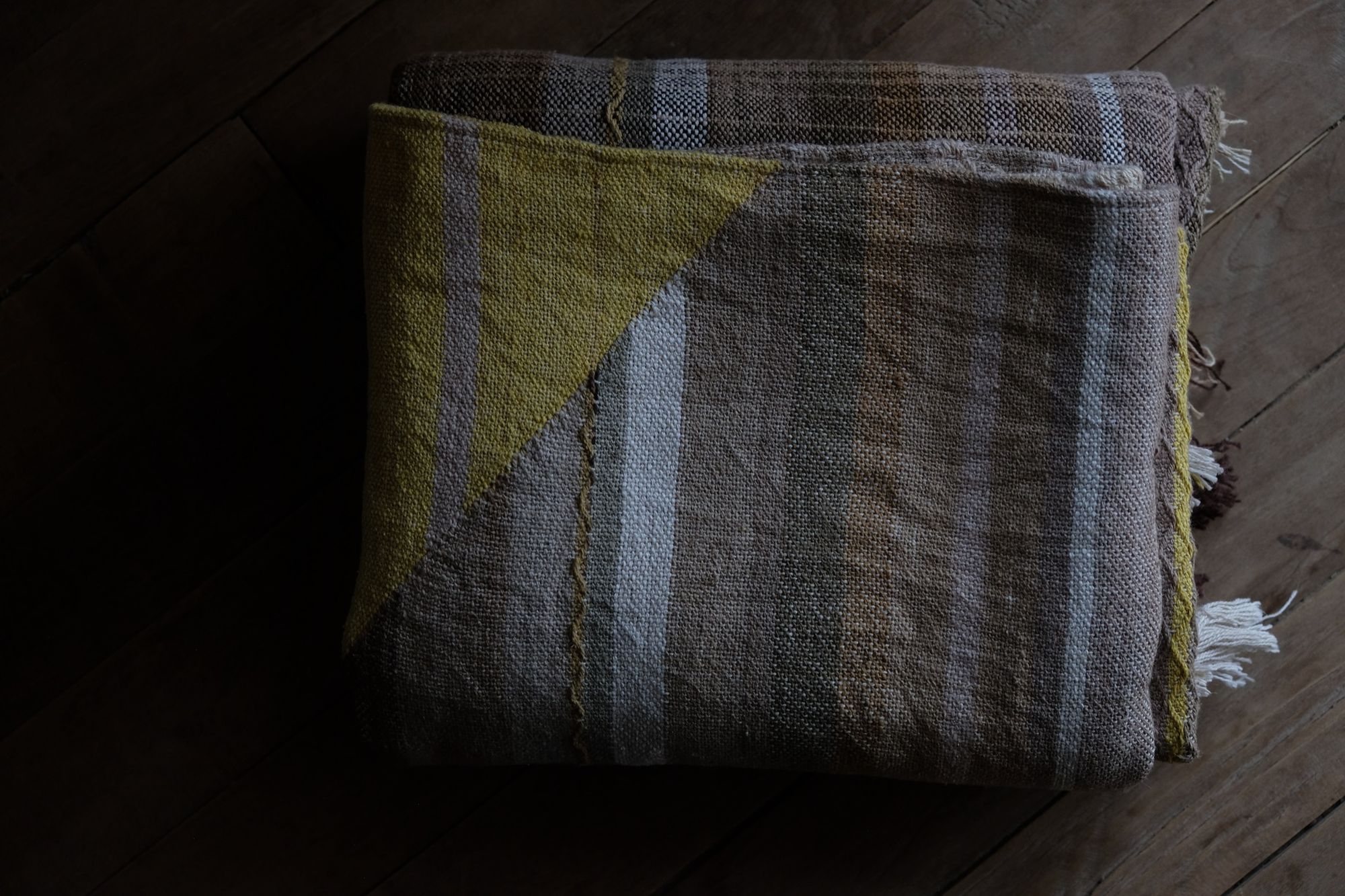 detail of handwoven diamond pattern and geometric details in browns, tan, yellows, whites and pinks laying on a wooden floor