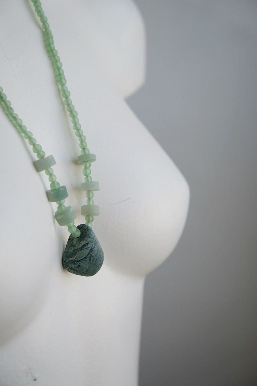 A white female form mannequin wears a necklace of a green ocean tumbled stone with green and black beads