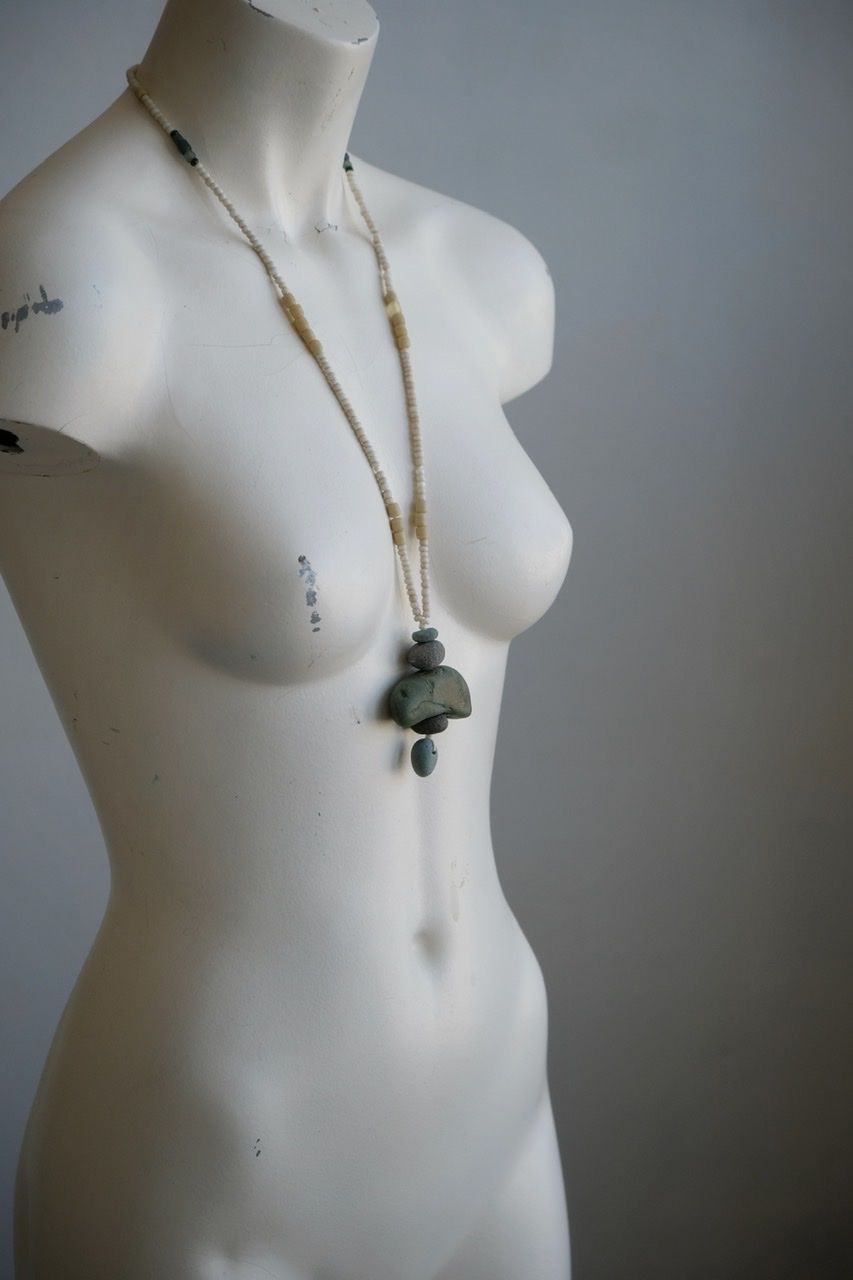 A white colored female form mannequin wears a sculptural necklace of blue green river tumbled stones and white glass beads