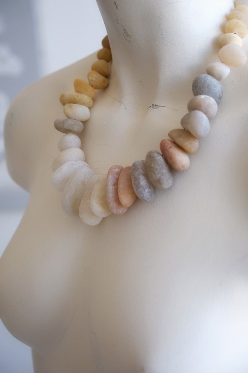 A white colored female formed mannequin wears a short necklace of ocean tumbled stones in white, grey, yellow, pale pink and red