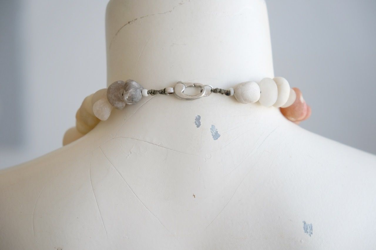 A white colored female formed mannequin wears a short necklace of ocean tumbled stones in white, grey, yellow, pale pink and red