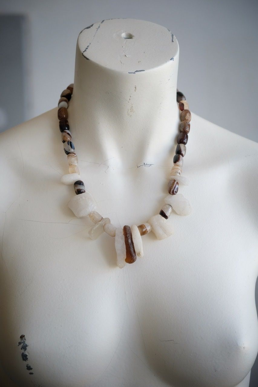 A white colored female form mannequin wears a white, clear and brown necklace of agate, Quartz and tumbled glass