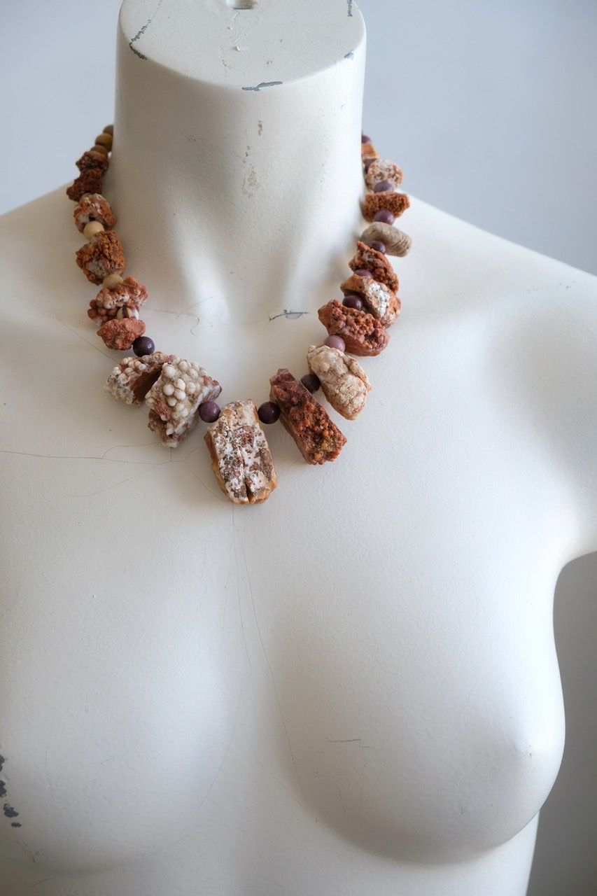 A white colored female form mannequin wears a snort necklace of orange botryoidal stones with yellow and purple jasper beads