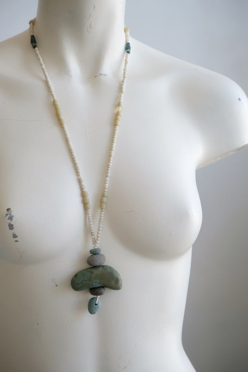 A white colored female form mannequin wears a sculptural necklace of blue green river tumbled stones and white glass beads